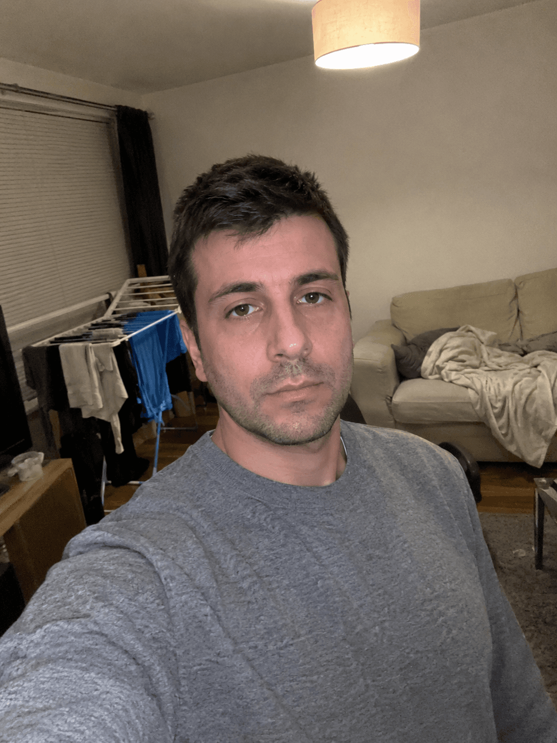 Man in a grey sweater in a cluttered living room, shot on a phone