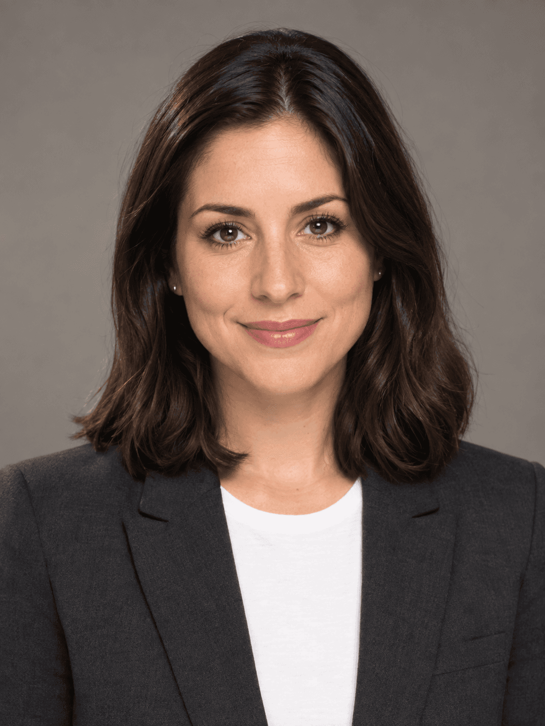 La stessa donna con blazer grigio antracite su fondo grigio caldo, luce da studio