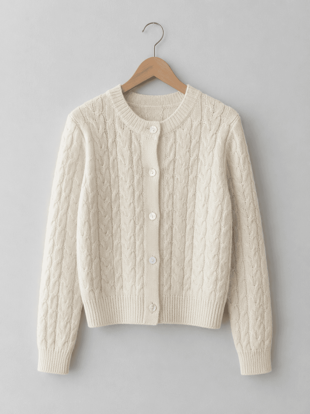 Lo stesso maglione color crema appeso a una gruccia davanti a una parete grigio chiaro