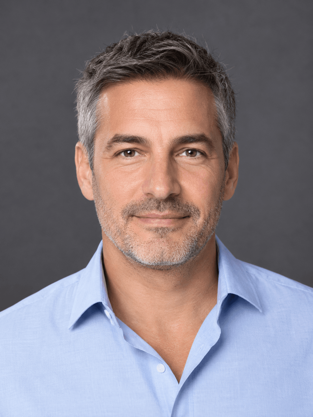 Portrait professionnel d’un homme aux cheveux courts grisonnants en chemise bleu clair sur fond gris ardoise