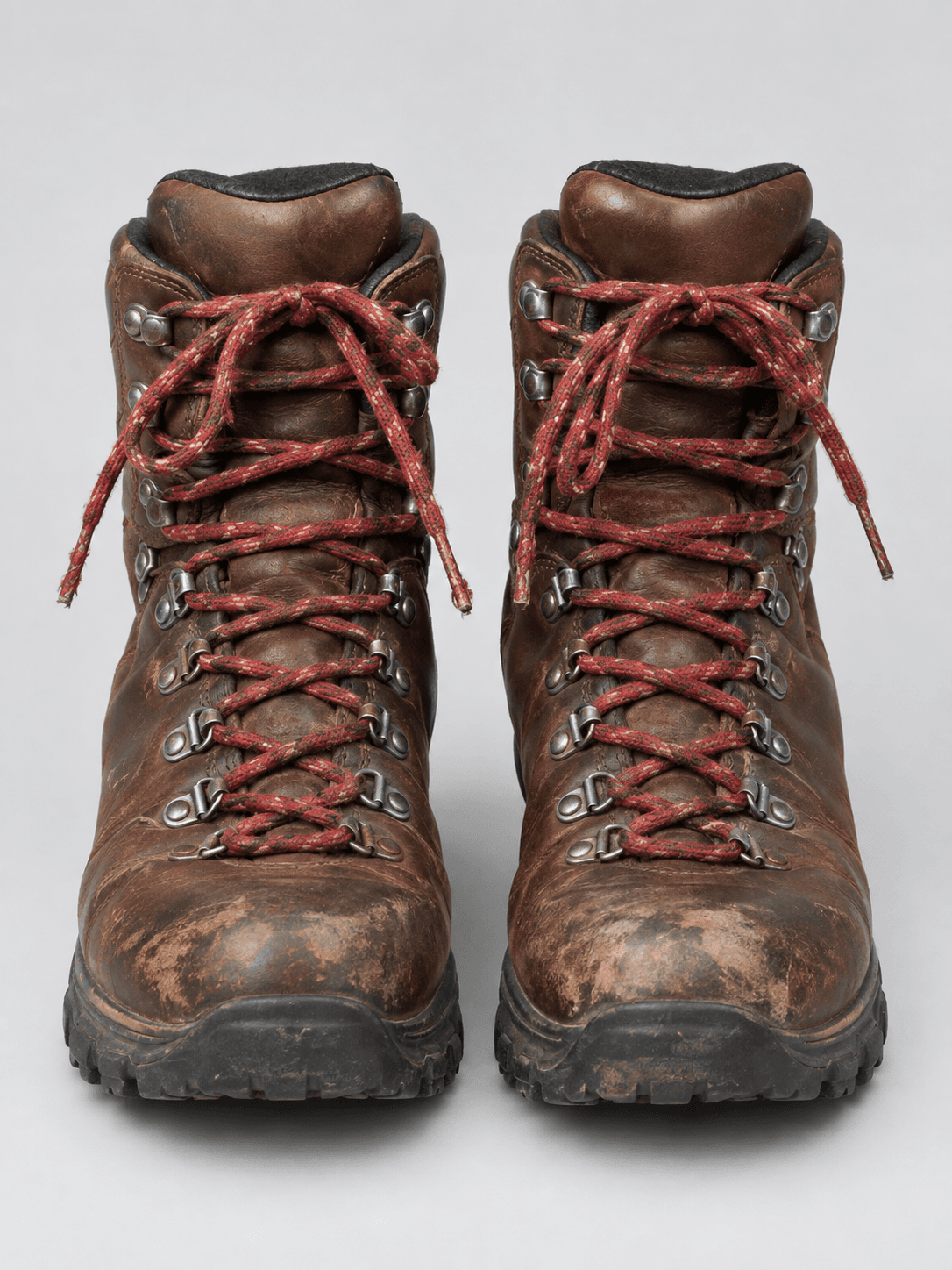 Gebrauchte braune Lederwanderschuhe mit abgescheuerten Kappen vor gleichmäßig hellgrauem Hintergrund