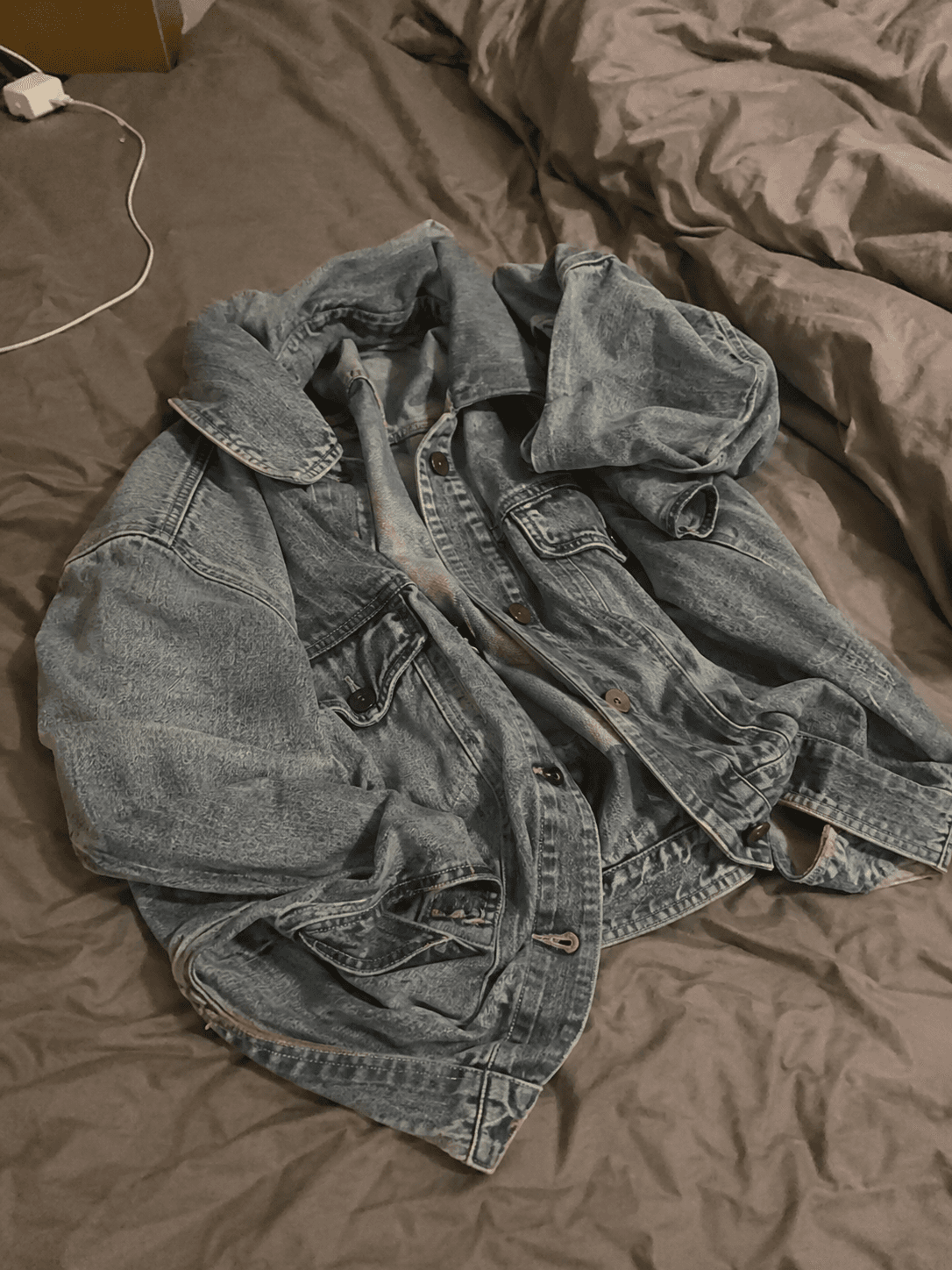Veste en jean bleu délavé froissée sur un lit défait, lumière artificielle jaune