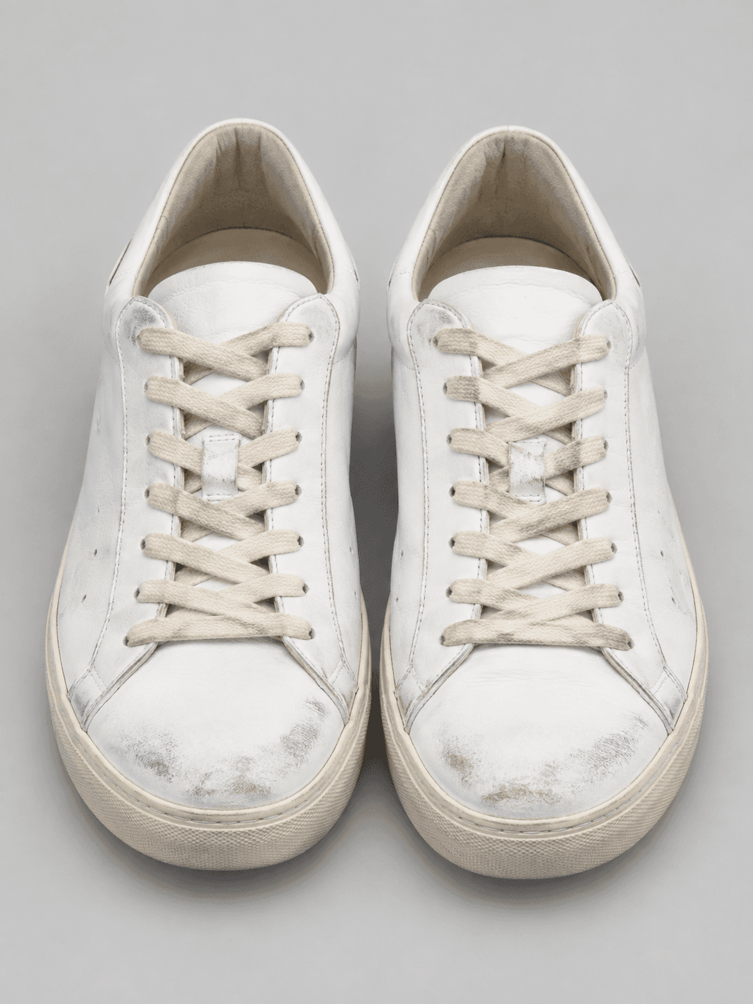 Paire de baskets en cuir blanc avec marques d’usure sur la pointe, sur fond gris clair uniforme