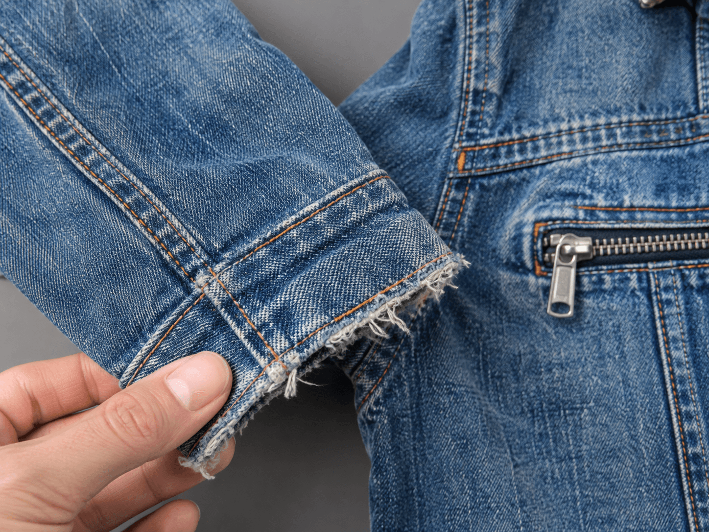 Gros plan sur le poignet effiloché et les coutures orange d’une veste en jean, tenue à plat