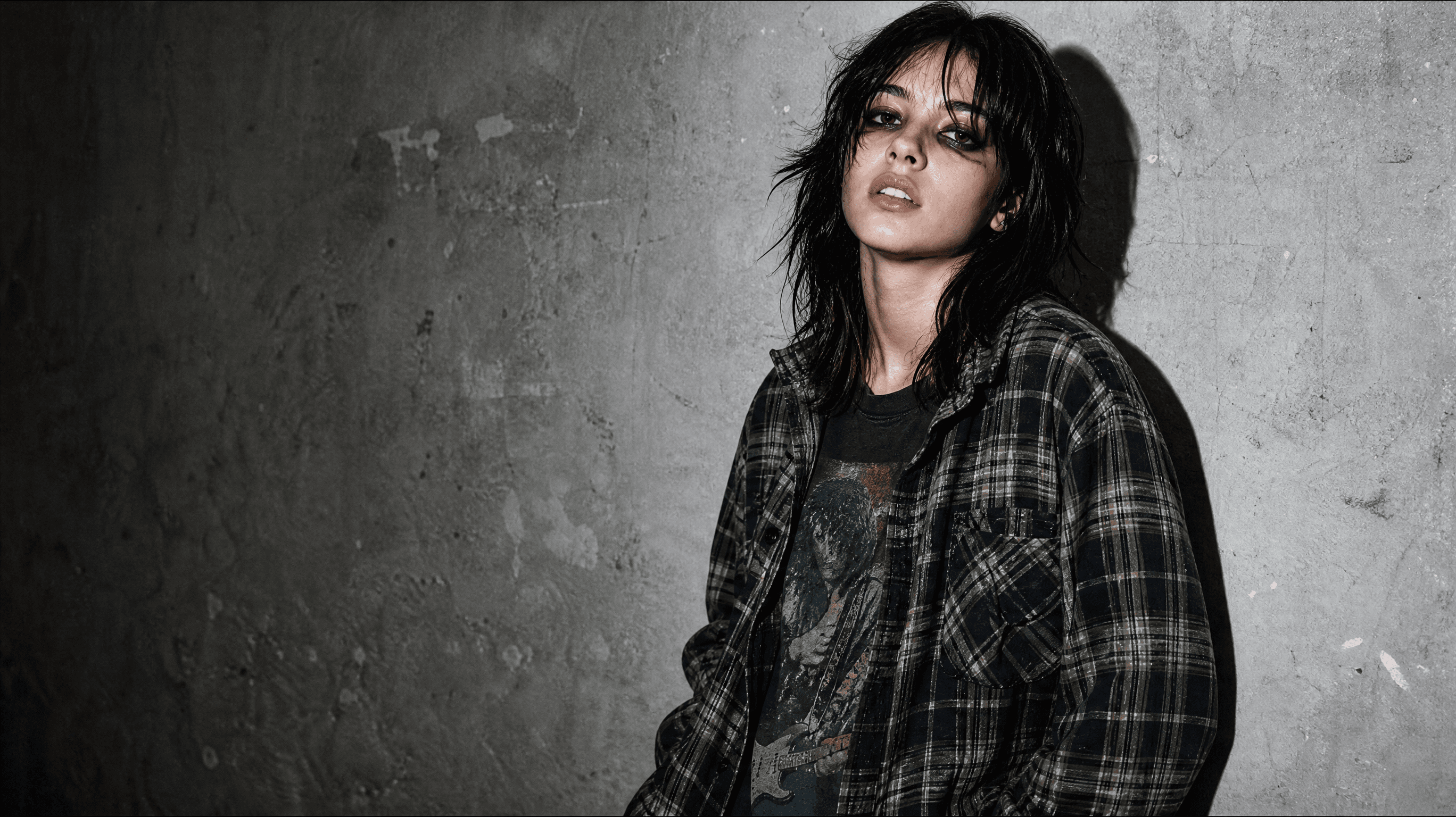Grunge portrait: young woman in an oversized flannel shirt against a concrete wall, hard flash and grain