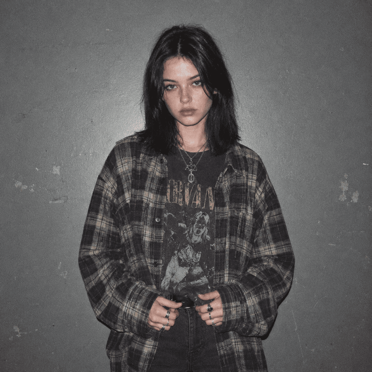 Grunge PFP: young woman in a flannel shirt over a tee against a grey wall